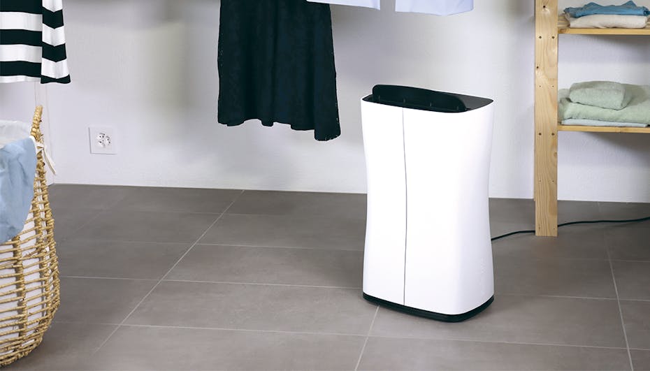 Osuszacz powietrza Stadler Form Theo stoi na podłodze w pralni, pod suszącymi się ubraniami