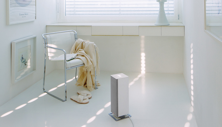 Termowentylator Anna big w białym kolorze stoi obok fotel w jasnym pomieszczeniu