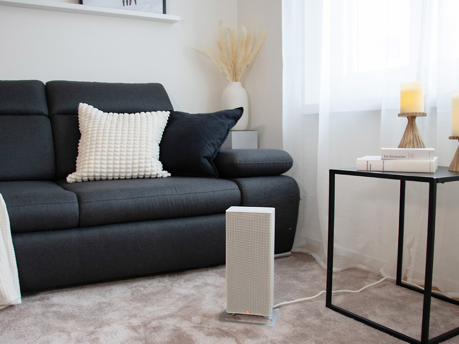 Termowentylator Stadler Form Anna stoi na miękkim dywanie przed szarą sofą